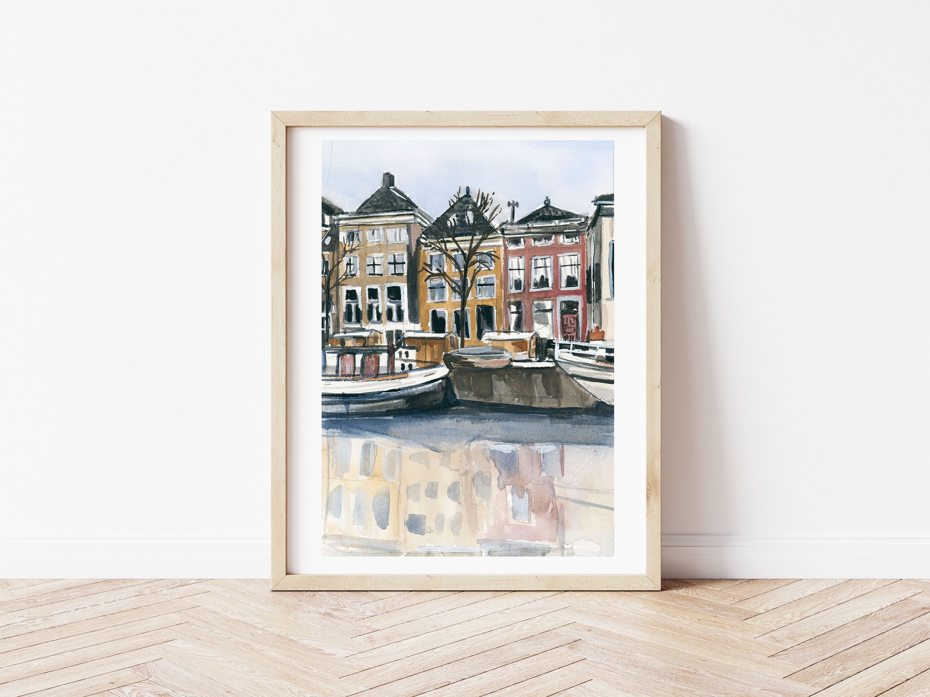 Amsterdam canal print of painting by Medjool Studio. Print of original gouache painting with brown, yellow and red building features behind small boats in the water from the Amsterdam canal.
