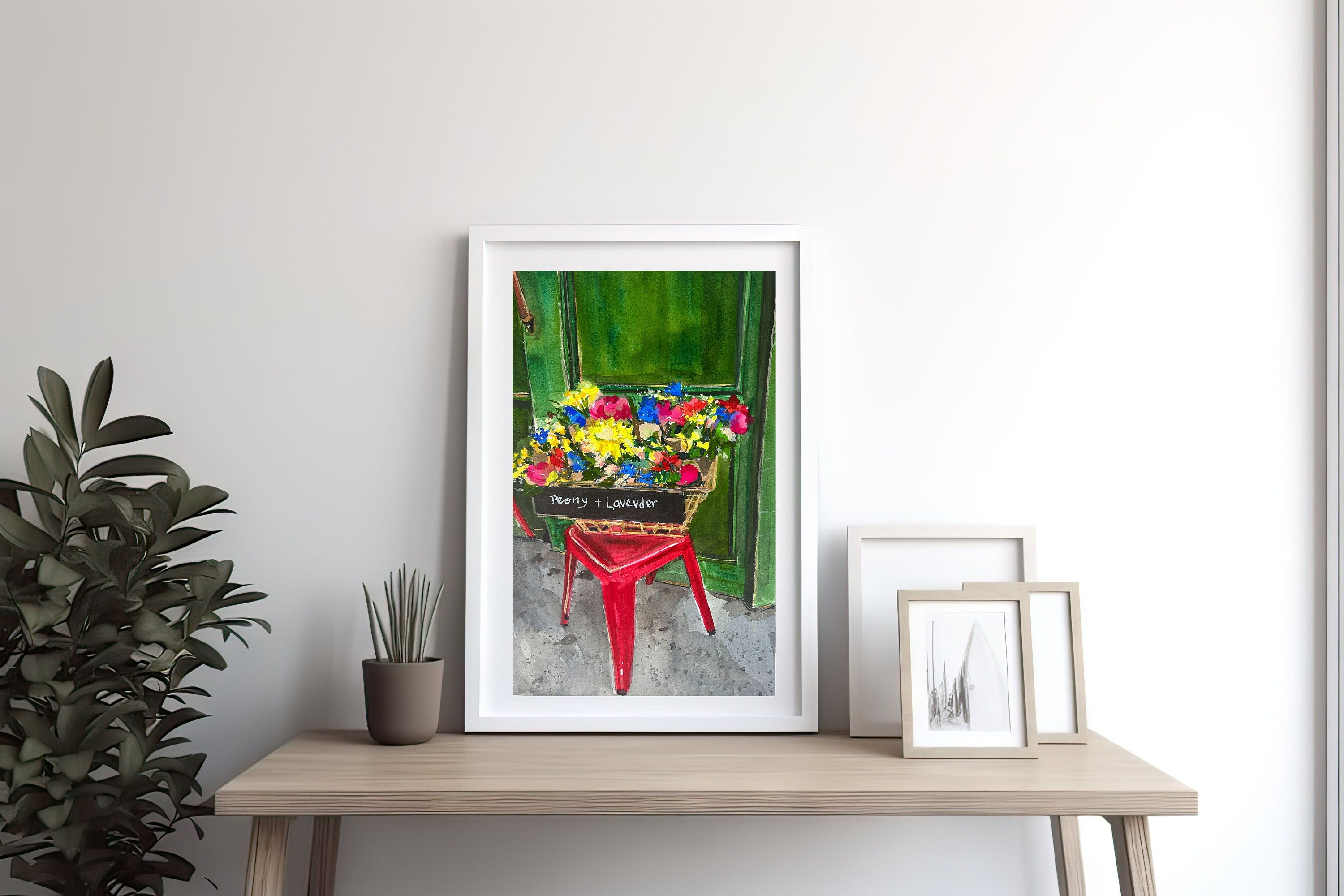 Flower market print of painting by Medjool Studio. Print of a watercolour painting of a basket of flowers on a small red stool on a side street in France.